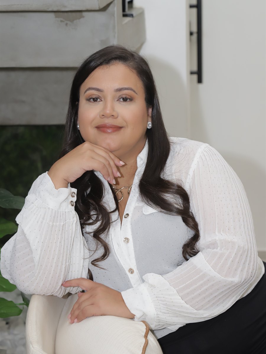 Psicóloga Flávia Santos de blazer verde-azulado, sorrindo em seu consultório